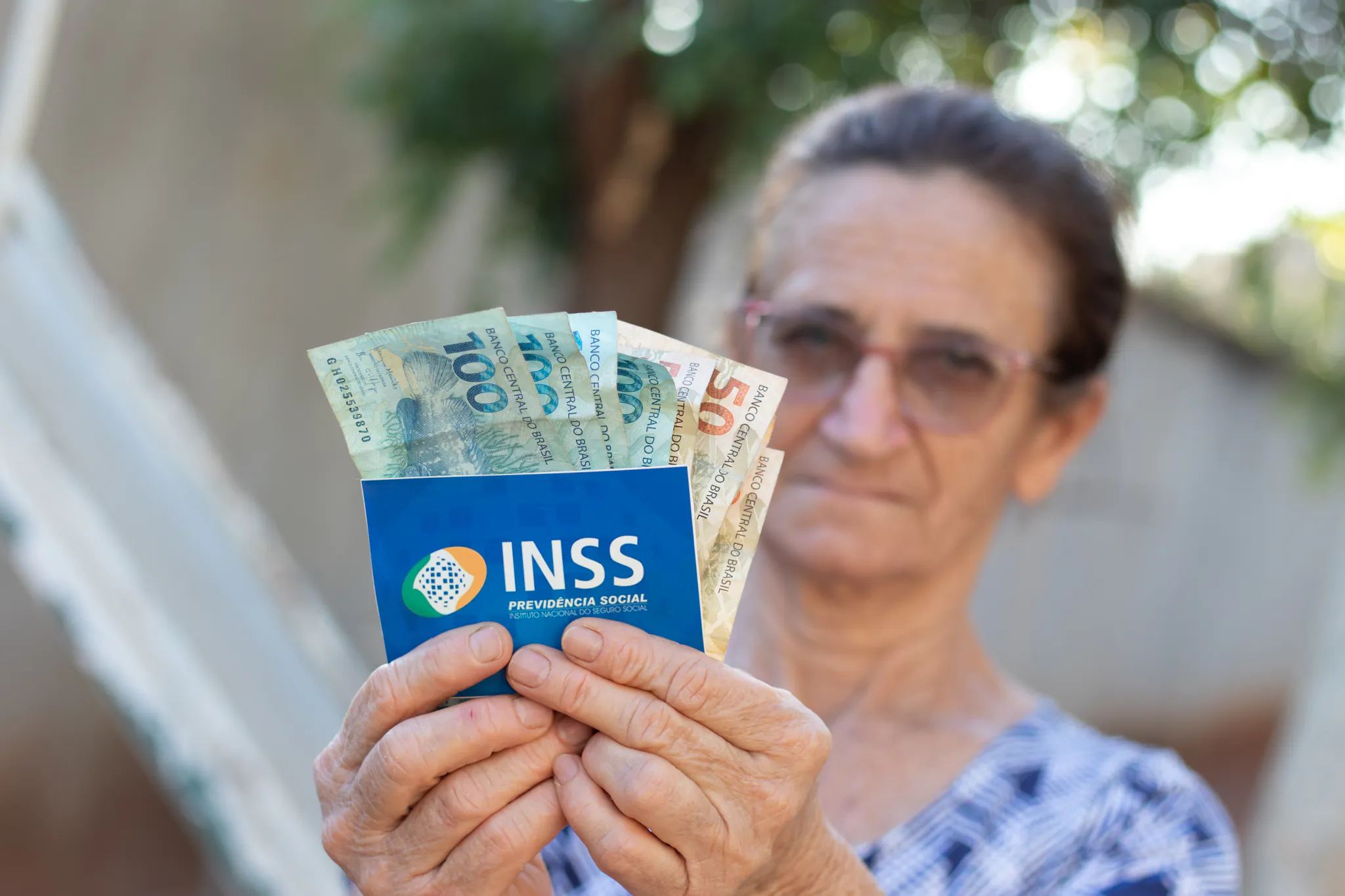 Aposentada feliz com o pagamento do abono extra e segurando dinheiro e cartão do INSS,