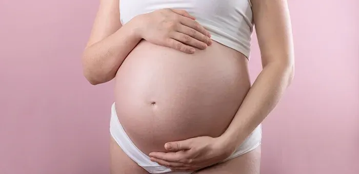mulher grávida vestida de branco com o fundo da parede rosa