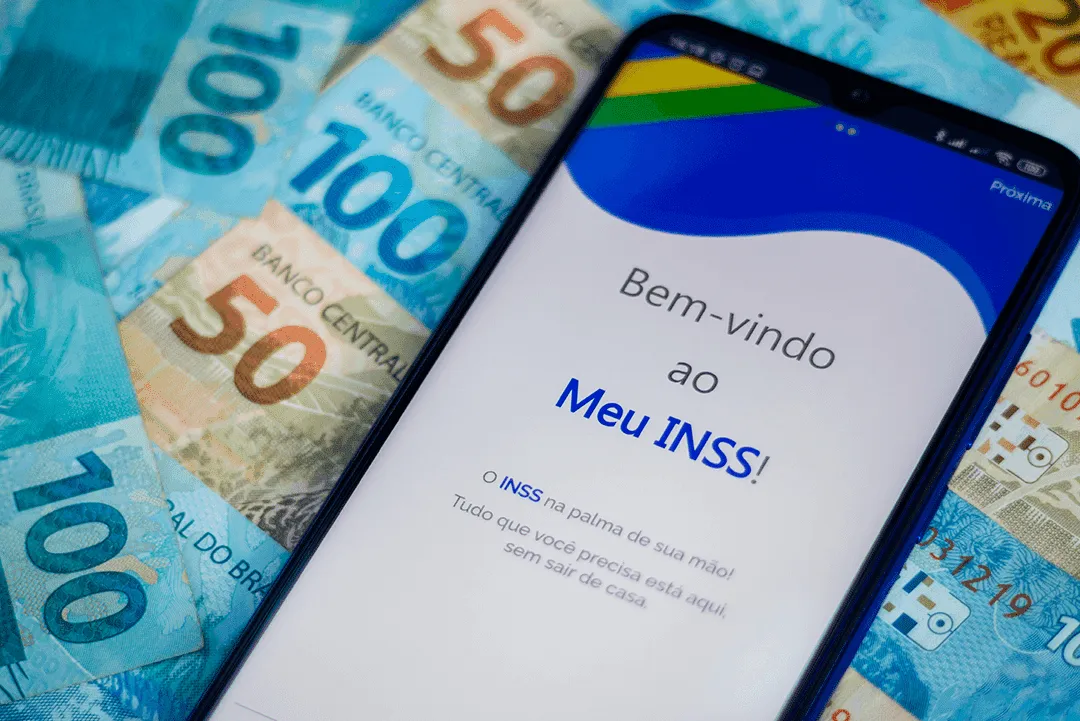 celular aberto no site do inss ao lado do pagamento feito com notas de 100 e 50 reais