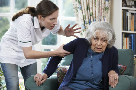 mulher sendo gritando e sendo violenta com uma idosa que está sentada numa poltrona azul e assustada